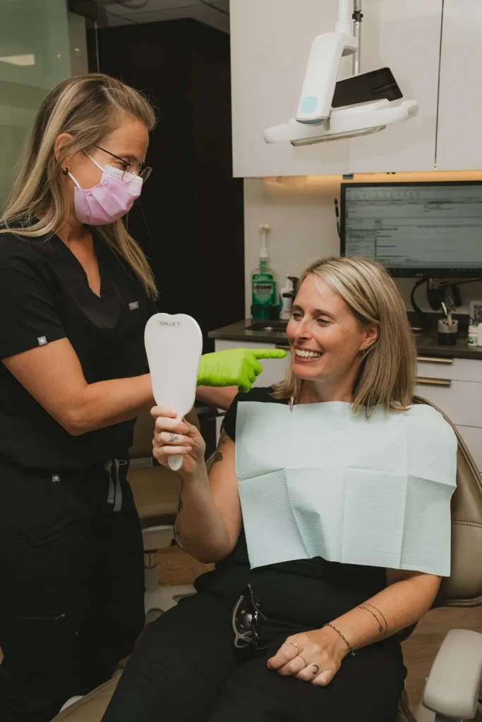 Dentiste présentant le résultat d’un traitement à une patiente à l’aide d’un miroir dentaire