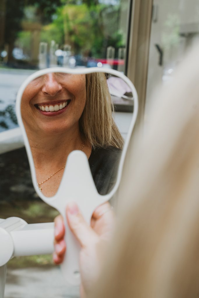 Patiente souriant devant un miroir après un traitement dentaire