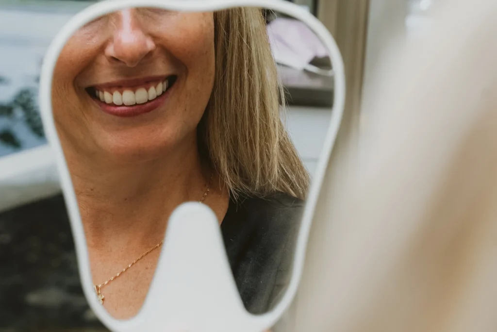 Patiente souriant en observant le résultat de son traitement dans un miroir dentaire