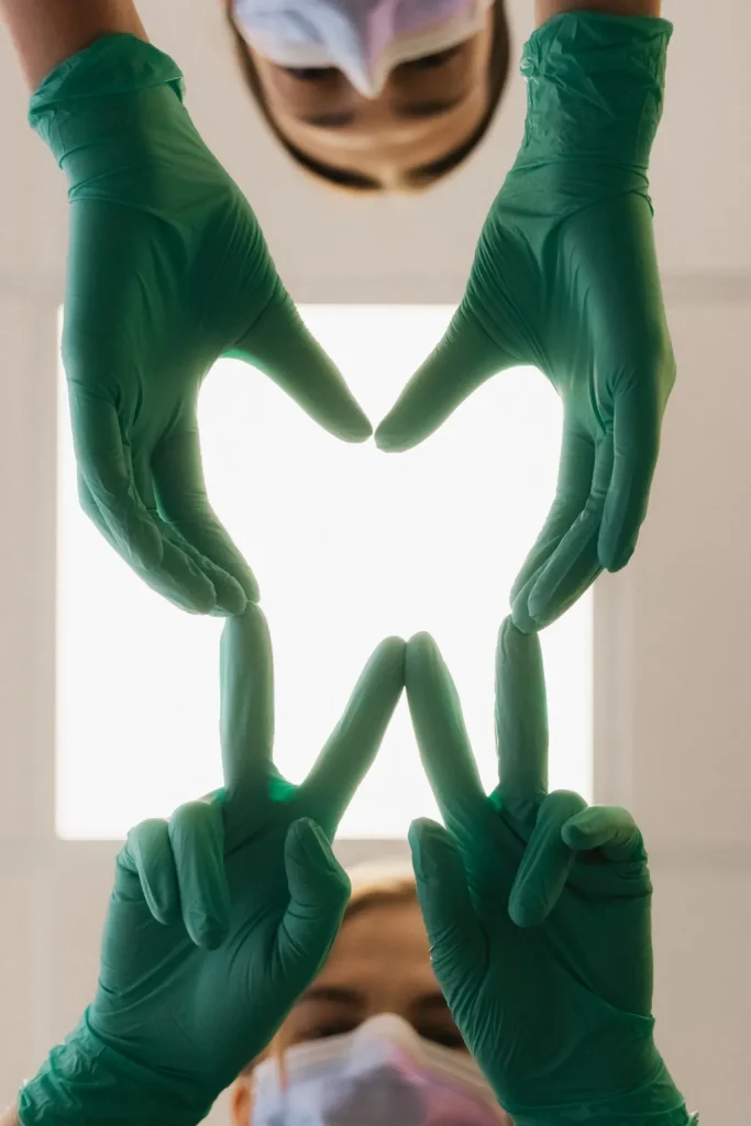 Équipe dentaire formant un sourire avec des gants médicaux au-dessus d’un patient en clinique dentaire